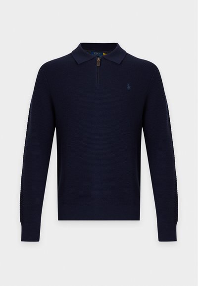 Pull tricoté bleu marine à manches longues avec une fermeture éclair devant, col et logo discret sur la poitrine gauche.