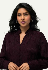 Maroon blouse with floral pattern, ruffled collar, and button-down front. Long sleeves and textured fabric. Circular earrings included.