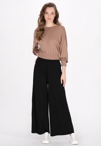 Crop top in tessuto marrone chiaro con maniche lunghe e orlo elasticizzato, abbinato a pantaloni neri larghi e sneakers bianche.