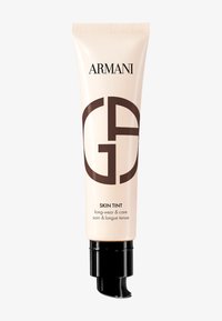 Beige tube med sort pumpe og låg. Har "Armani"-logoen og "Skin Tint"-teksten i brun. Glat, blank finish; strømlinet design.