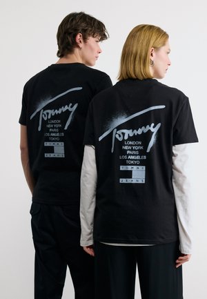 Two people facing away wearing black Tommy Jeans t-shirts with city names London, New York, Paris, Los Angeles, Tokyo printed in white.