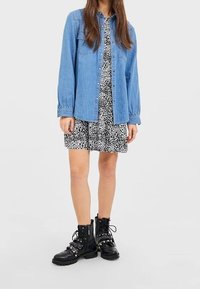Chemise en denim à boutons portée sur une robe à imprimé léopard noir et blanc, associée à des bottes de combat noires avec des clous et des lacets.
