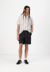 Kortermet skjorte med knapper og flerfargede striper, sammen med svarte shorts med elastisk linning og svarte joggesko med hvite detaljer.