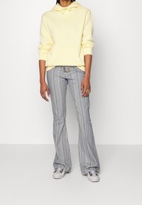 Žlutá bavlněná mikina s kapucí a klokaní kapsou, doplněná modrými a bílými pruhovanými rozšířenými kalhotami. Obuv tvoří světle šedé tenisky.