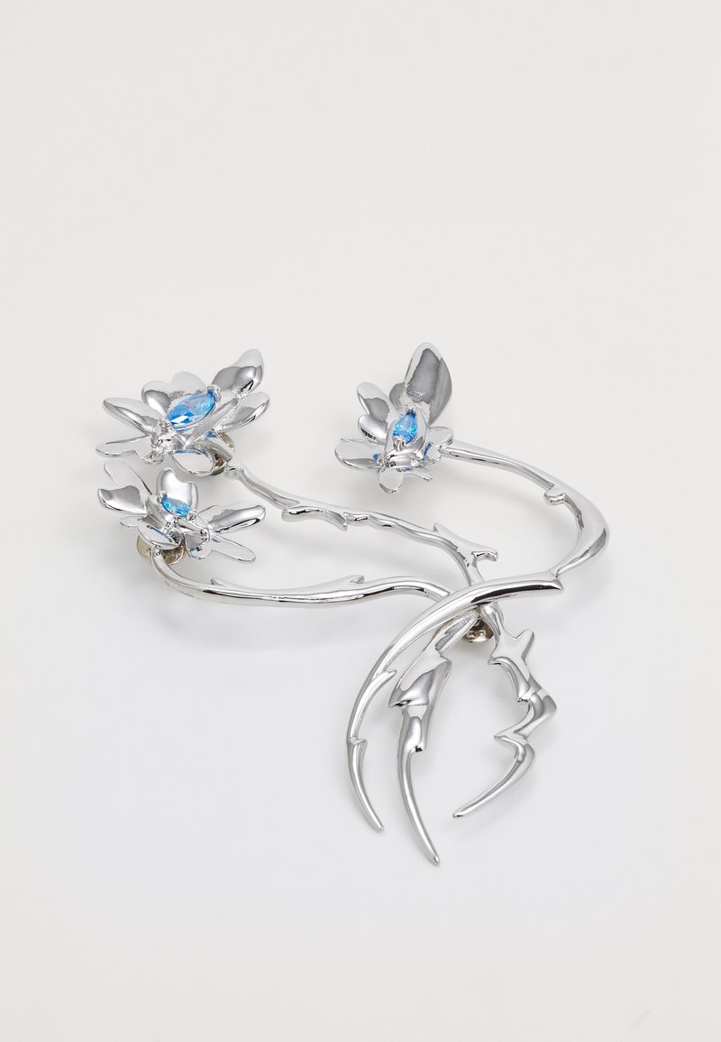 Srebrna broš van oblikovana poput grančica s tri cvjetna akcenta, sa svijetloplavim gemovima u središtu, poliranom površinom i organskim detaljima dizajna.