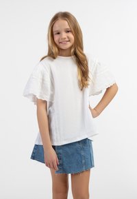 Hvid tekstureret bluse med korte, løse ærmer, der har hulmønster i kanterne. Sættes sammen med en lys blå denimnederdel.