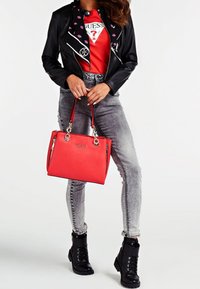 Czarna kurtka z sztucznej skóry z białymi przeszyciami, czerwona torebka, szare legginsy skinny z zamkami oraz czarne sznurowane botki za kostkę.