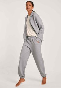 Lichtgrijze zip-up jas met een opstaande kraag, gepaard met bijpassende joggerpants. Beide zijn gemaakt van zachte stof, met zakken en elastische boorden.