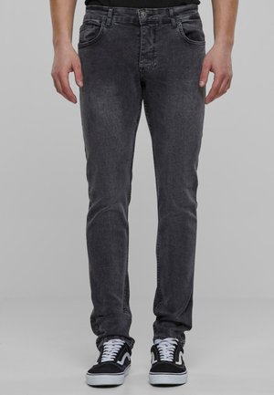 Dark gray denim jeans with a slim fit, featuring five pockets, belt loops, and subtle fading. Paired with black and white sneakers.