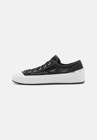 Svarte nett sneakers med en tykk hvit plattformsåle og sølvfarge aksent ved hælen, med svarte snøringer og hull.
