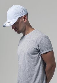Világoskék sapka ívelt karimával és ezüst hardware-rel. Szürke rövid ujjú póló, puha, textúrált anyagból. Egyszerű, hétköznapi design.