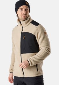 Fleece jacket in beige with black accents and zip pockets. Features high collar and textured fabric. Includes logo patch on shoulder.