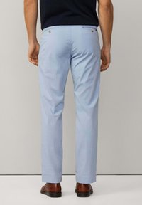 Ljusblå dressbyxor med en slät yta, två bakfickor med knappstängningar och rakt ben-design, i kombination med bruna skor.