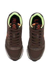 Une paire de baskets marron avec une doublure intérieure néon verte, un texte orange "COURIR PLUS VITE QUE VOUS NE POUVEZ" sur la languette, et des semelles intérieures noires avec des lettres rouges.