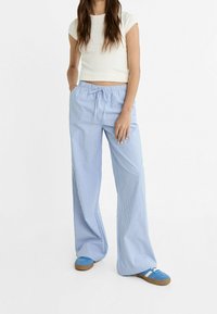 Pantalons larges rayés bleu clair avec une taille élastique et un cordon de serrage. Associés à un haut ajusté blanc à manches courtes et des chaussures bleues.