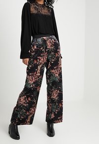 Czarna bluzka z długim rękawem z koronkową nakładką oraz szerokie spodnie w kwiatowy wzór w ciemnych tonach, z żywym kwiatowym motywem i elastycznym paskiem w talii.