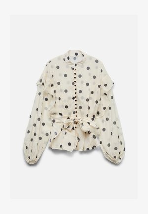 Blouse crème à pois noirs, détails à volants, boutons en forme de cœur, manches longues bouffantes et nœud à la taille.