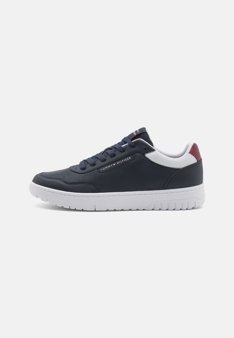 Marinblå lädersneaker med vit sula, utrustad med vadderad krage, snörningsdesign, röd detalj vid hälen och en logotyp på sidan.
