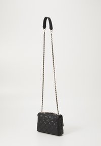 Borsa in pelle trapuntata nera con una tracolla a catena e un manico nero solido. Presenta una forma rettangolare e una chiusura a pattina con dettagli decorativi.