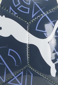 Puma futbolo kamuolys su blizgiu tamsiai mėlynu paviršiumi, papuoštas baltu logotipu ir šviesiai mėlynomis geometrinėmis figūromis, siuvinėtas ryškiai žalia siūle.