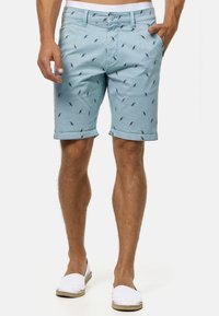 Light blue shorts made of cotton with a smooth texture, featuring a repeated bird print design. Rolled cuffs and standard button closure.