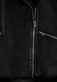 Veste noire en mélange de cuir et de daim, zip en argent, deux poches avant zippées et doublure intérieure douce et texturée.