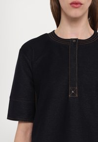 T-shirt en mélange de coton bleu marine avec des manches courtes, patte de boutonnage et surpiqûres contrastantes orange le long du col et de l'ourlet.