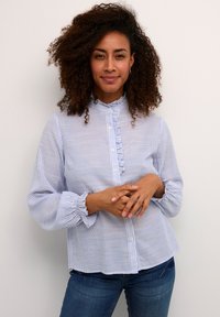 Chemise boutonnée à rayures bleu clair et blanche avec un col et des poignets volantés. Le tissu semble doux ; les manches sont amples et resserrées.