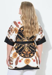 Kimono s květinovým vzorem v bílé, černé a zlaté barvě, se krátkými rukávy, s úzkým pasem zdůrazněným černým pásem a lehkým materiálem.