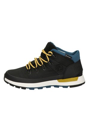 Zapatilla media alta de textil negro con cordones amarillos, cuello de tobillo azul, entresuela blanca y suela de goma negra con un patrón texturizado.