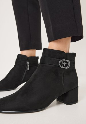 Bottes noires en daim jusqu'à la cheville avec un talon bloc, dotées d'une fermeture éclair sur le côté, d'une boucle décorative et d'une finition lisse et texturée.