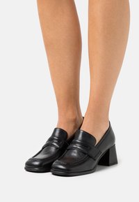 Sorte læder sko med blokhæl og rund tå, med et penny loafer-design og syddetaljer. Glat tekstur, minimal pynt.