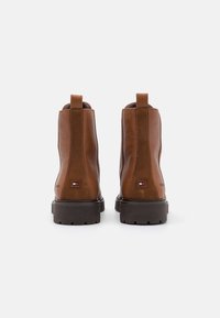 Botas de tobillo de cuero marrón con un acabado texturizado, paneles laterales elásticos, lengüetas de tiro y una suela de goma contrastante. Detalle del logo icónico visible.