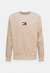 Kerman värinen pitkähihaisesta corduroysweatshirtista, jossa on ribbaböljy- ja helmaosat, ja rintakehässä pieni Tommy Jeans -logo.