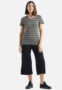 Young woman standing, wearing a gray short-sleeve striped shirt, black wide-leg cropped pants, and black sneakers on white background.