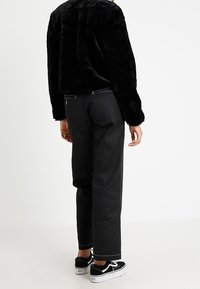 Svart faux fur-jacka, lös passform. Svarta byxor med vit stickningdetalj, rak klippning. Svarta sneakers med vita sulor.