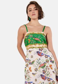 Abito maxi con un corpetto a fantasia verde, che presenta uccelli e fiori colorati su uno fondo bianco. Spalline sottili e tessuto texturizzato.