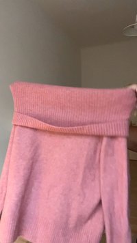 Rózsaszín kötött pulóver széles, bordázott, vállra húzható nyakkivágással, puha textúrával és laza szabással.