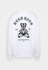 Sweat blanc avec un motif ours noir de style tribal, texte « HUGO » au-dessus, texte « WORLDWIDE ORIGINAL 1993 » en dessous, et petit texte additionnel.