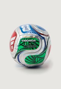 Replika lopte za FIFA utakmicu s metalnim površinom i apstraktnim uzorcima u crvenoj, plavoj, zelenoj i bijeloj boji te logotipima na jednostavnoj pozadini.