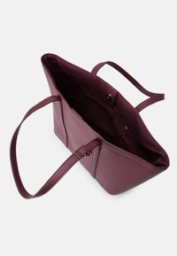 Burgundy színű műbőr bevásárlótáska, két hosszú füllel, nyitott tetejű, belső cipzáros zsebbel. Simább textúra, minimális varrási részletekkel.