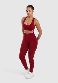Rode sportbeha en hoge taille legging set gemaakt van rekbaar materiaal; gladde textuur, aansluitend ontwerp en prominente naden. Witte sneakers gedragen.