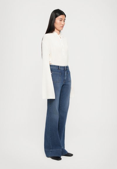 Top bianco a maniche lunghe con colletto, abbinato a jeans a campana blu scuro a vita alta; design minimalista, texture liscia.