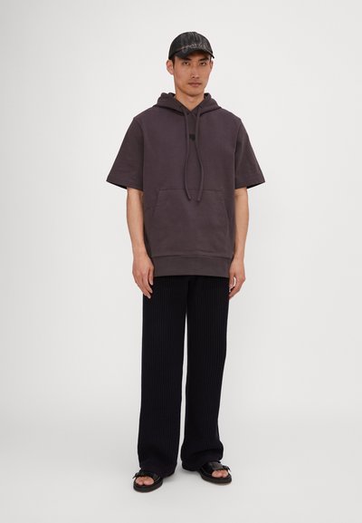 Oversized mørkegrå hettegenser med frontlomme, kombinert med ribbestrikkede svarte vidde bukser og mørke sandaler. Enkelt design med minimale detaljer.