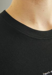 Sort bomulds t-shirt med ribbet rund halsudskæring. Glat tekstur og korte ærmer, med hvidt trykt tekst nær kanten.