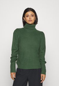 Temno zelena rebrasta turtleneck pulover s dolgimi rokavi in prilegajočimi manšetami, z diskretnim teksturiranjem in tesnim prileganjem okoli ovratnika.