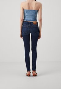 Denim korsettopp kombinerat med mörkblå skinny jeans. Jeansen har en klassisk femfickdesign och en märkesläderpatch på baksidan.
