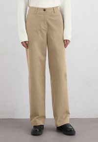 Pantalons larges beiges en coton. Comprend une fermeture à bouton, des poches avant et une coupe décontractée. Associés à des bottes noires.