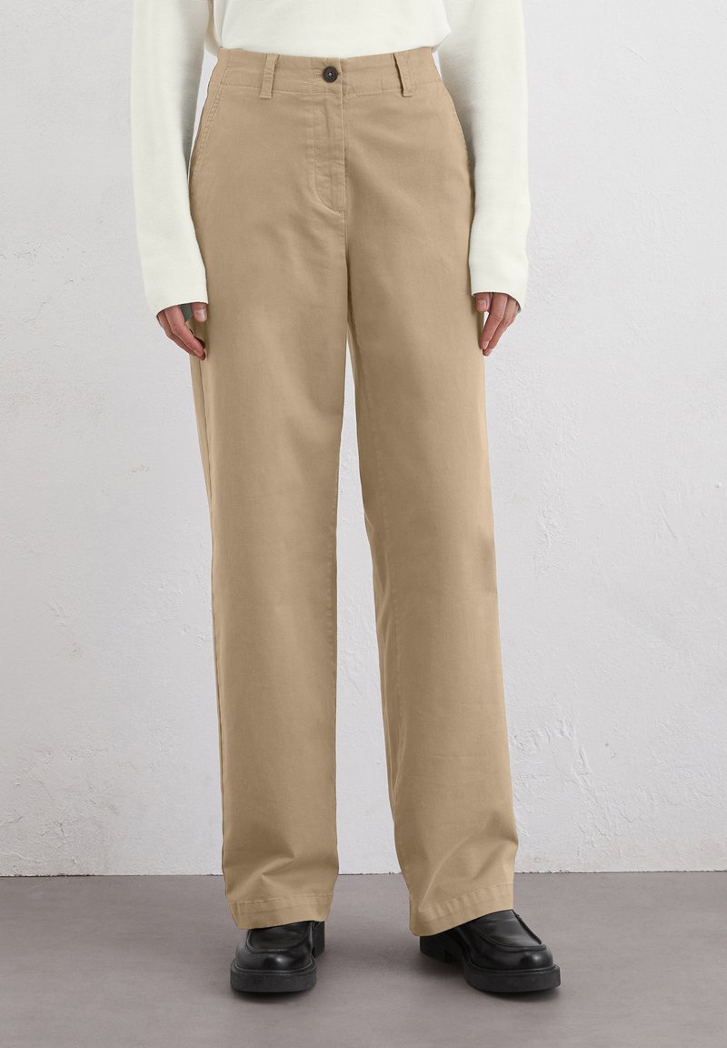Pantalons larges beiges en coton. Comprend une fermeture à bouton, des poches avant et une coupe décontractée. Associés à des bottes noires.