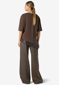 Brūna p�ārliela izmēra T-krekls ar īsām piedurknēm, ar mežģīņu apakšmalu. Kombinēts ar vaļīgām tumši olīvu zaļām plaša kāju biksēm ar gludu tekstūru.